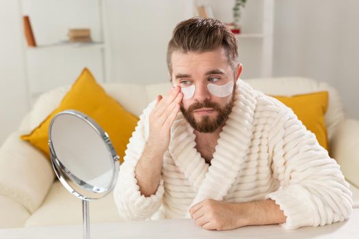 Bearded man applying eye patches on his face. Wrinkles and face home care for men.