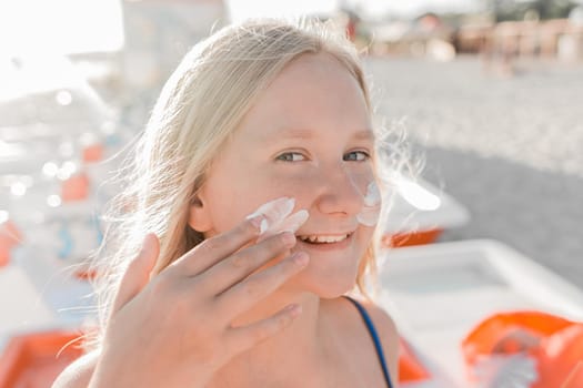 Close-up portrait of a young sweet and happy teenage girl smearing sunscreen on her face