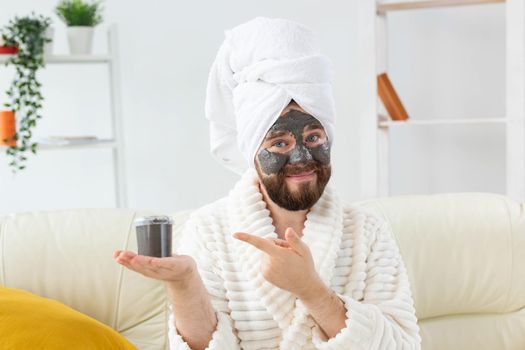 Bearded man having fun with a cosmetic mask on his face made from black clay. Men skin care, humor and spa at home concept