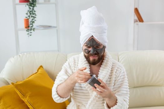 Bearded man having fun with a cosmetic mask on his face made from black clay. Men skin care, humor and spa at home concept