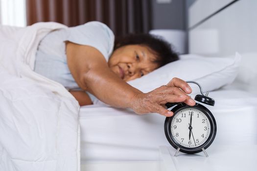 senior woman in bed pressing snooze button on morning alarm clock 