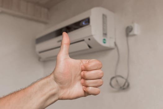 The guy's hand shows the class thumbs up against the background of the air conditioner on the wall in the room background