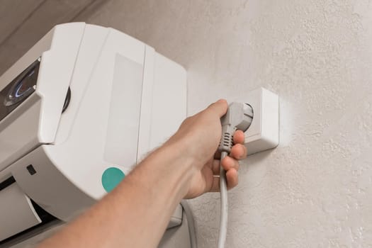 The hand disconnects or plugs the air conditioner power plug on the wall in the room from the outlet
