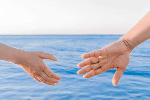 The man's hand reaches for the woman's hand against the background of the sea. Romantic Relationships and Friendship Concept