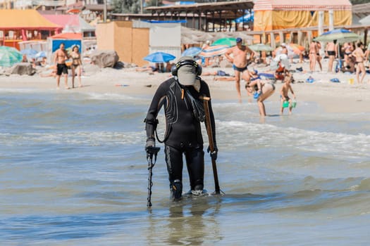 A man with a special device and equipment metal detector looking for lost jewelry and gold in sea water near the beach
