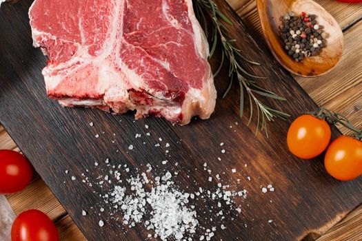 Raw T-bone steak with herbs on wooden board