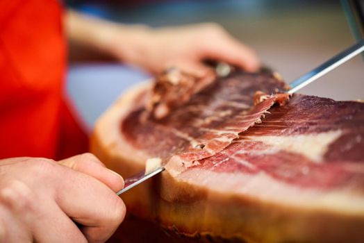 Professional cutter carving slices from a whole bone-in serrano ham