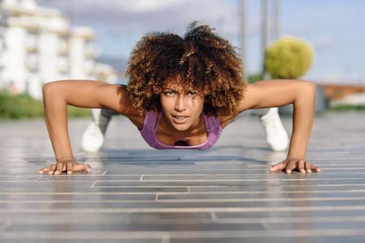 Black fit woman doing pushups on urban floor.