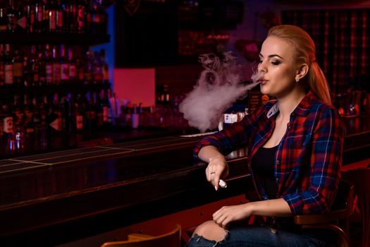 Young pretty woman smoke an electronic cigarette at the vape bar