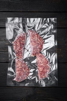 Vacuum beef or lamb mutton cutlet sealed airtight pack, on black wooden table background, top view flat lay