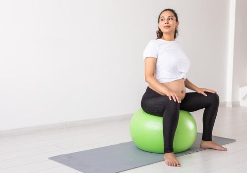 A young pregnant woman doing relaxation exercise using a fitness ball while sitting on a mat. Copyspace
