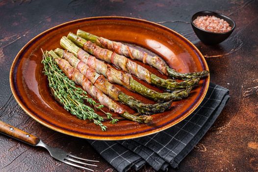 Grilled green asparagus wrapped with bacon on a plate. Dark background. Top view