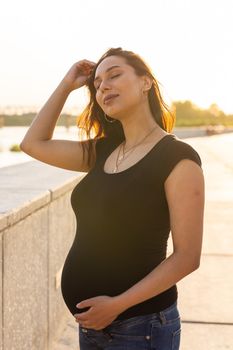Pregnant hispanic woman on embankment, touching belly