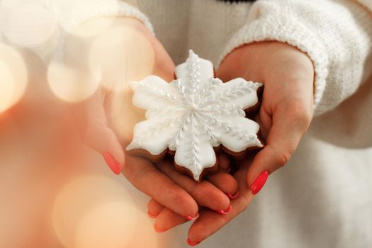 Hand of a woman in festive sweater holding gingerbread cookie with blurred lights