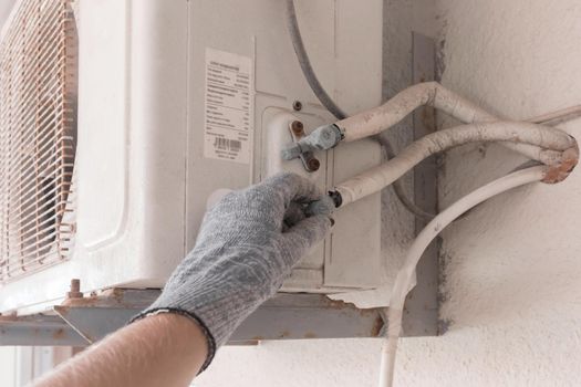 The hand of an air conditioner repair and maintenance specialist in a construction glove working with air-conditioned old equipment