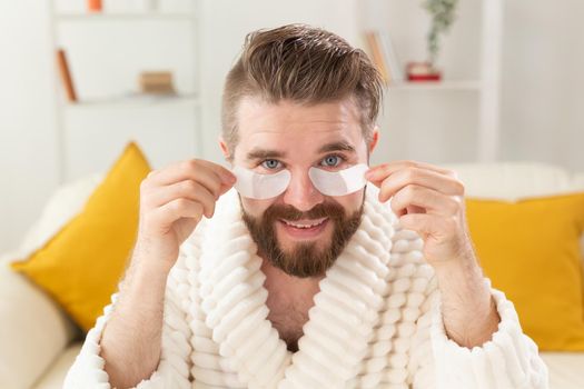 Bearded man removing eye patches on his face. Wrinkles and face home care for men.