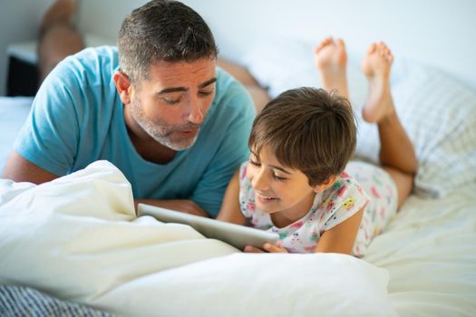 Middle-age father with her eight years daughter using digital tablet in bedroom.
