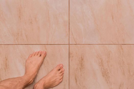 Bare feet man barefoot stands on the tile floor background, top view
