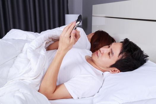 man using his mobile phone in bed while his wife is sleeping next to him