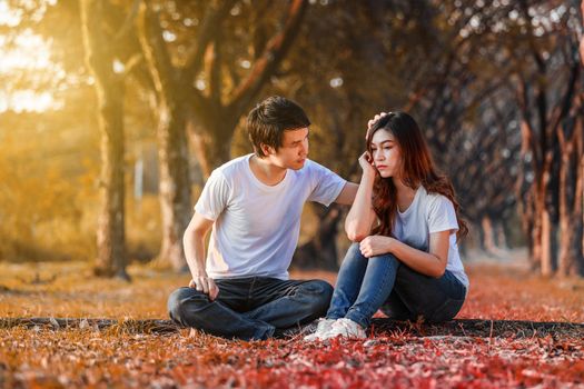 unhappy woman sitting with a concerned guy comforting her in park