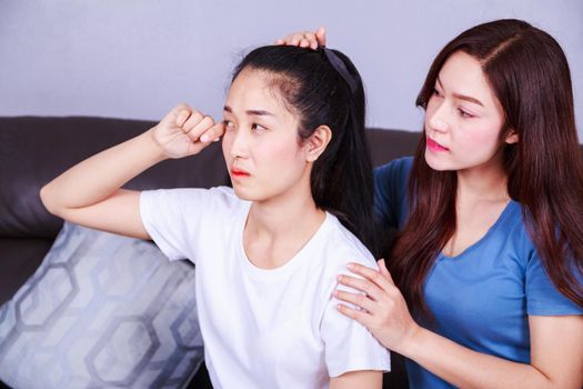 woman crying, her friend is calming her. on sofa at home