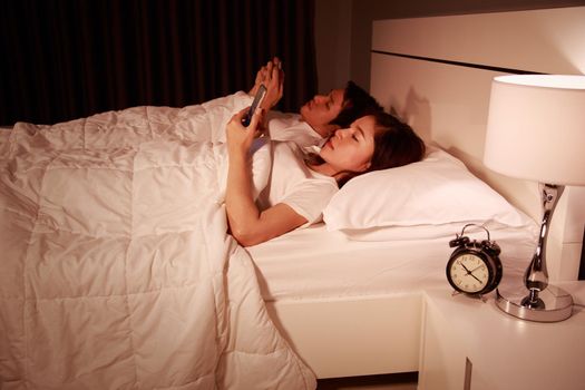 couple using mobile phone on bed at night