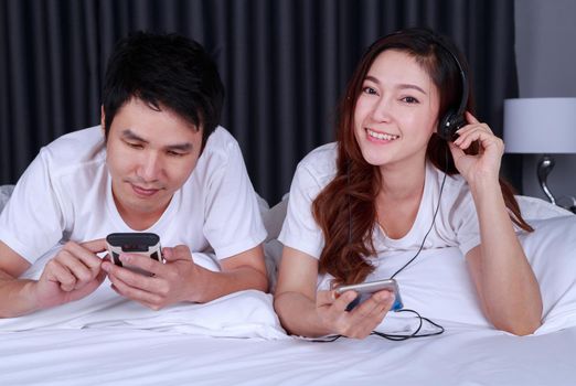 couple listening music from mobile with headphone on bed