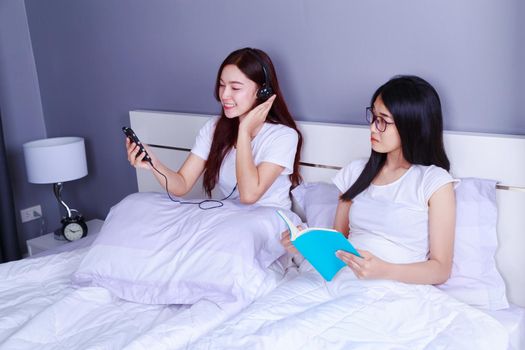 two woman reading a book and using smart phone on bed in bedroom