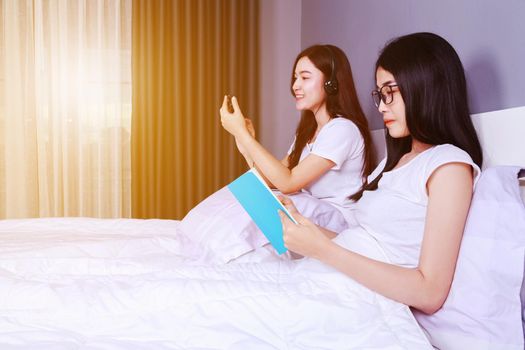 two woman reading a book and using smart phone on bed in bedroom