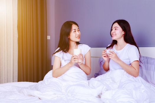 two best friends talking and drinking a cup of coffee on bed in bedroom 