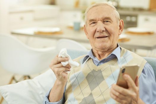 Elderly sick man sitting on the couch and holding a phone