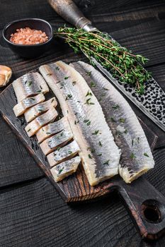 Sliced salted herring fish fillet on a wooden board. Black wooden background. Top view