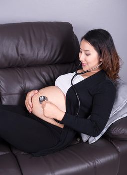 pregnant woman listening baby's heartbeat with stethoscope on her belly