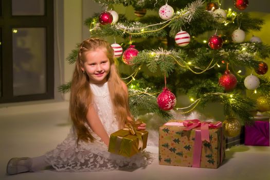 Little girl near the Christmas tree with a gift.