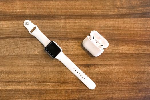 Belarus, Minsk region - March 17, 2020: Apple Watch 4 and AirPods headphones on wooden texture table background