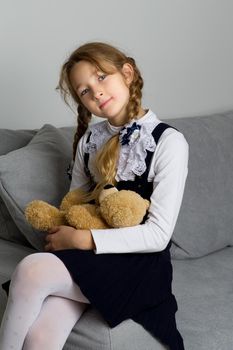 Cute schoolgirl sitting on sofa with teddy bear