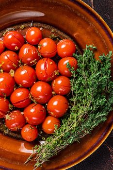 Marinated Preserve cherry tomatoes in a rustic plate with garlic and thyme. Dark background. Top view