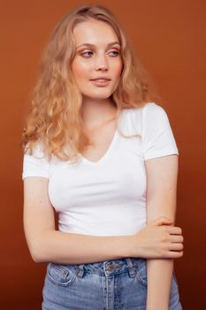 young pretty girl with blond curly hair posing cheerful on brown background, lifestyle people concept