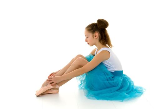 Adorable little girl putting on her ballet dancing shoes, sitting on the floor at a dance studio. Little ballerina is preparing for classes in a ballet school, copy space. Achievement, concept of dedication