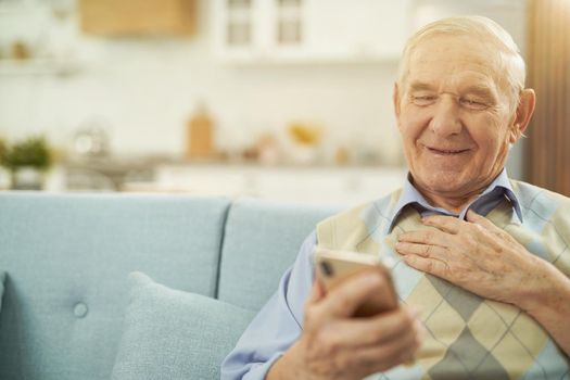 Smiling old man looking at phone screen at home
