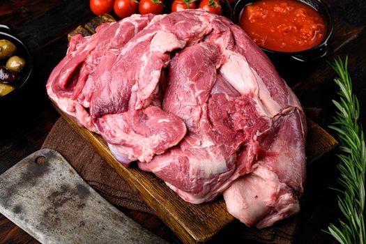 Fresh raw mutton shoulder meat, with ingredients and herbs, on old dark wooden table background