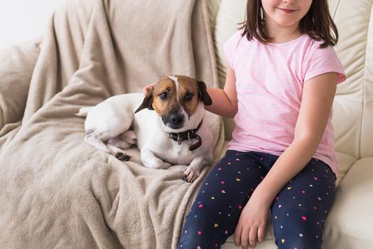 Child girl with cute dog jack russell terrier on the couch. Pets and home.