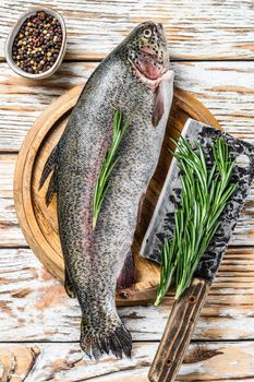 Rainbow trout on an wood board, with rosemary and cleaver. White wooden background. Top view