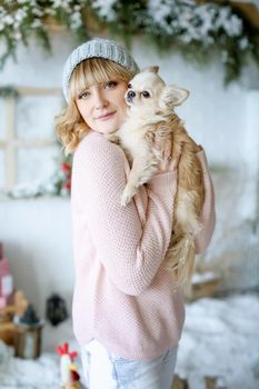 A woman 25-30 years old in a cap and pink sweater holding a pet Chihuahua