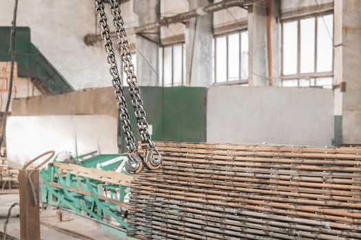 Lifting mechanism of an overhead crane with a hook and chain next to the reinforcement of iron structures in a workshop of an industrial enterprise