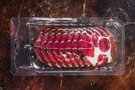 Italian sliced cured coppa meat in vacuum packaging. Dark background. Top view