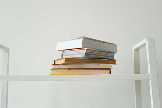 Books standing on a white rack at home. Knowledge, study and literature concept.
