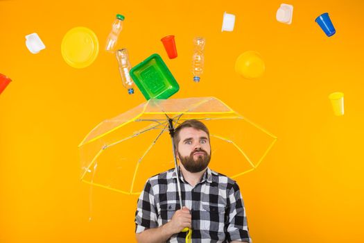 Problem of trash, plastic recycling, pollution and environmental concept - Sad man is standing under trash with umbrella on yellow background