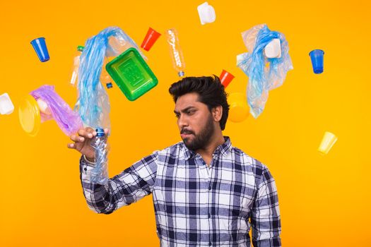 Plastic recycling problem, ecology and environmental disaster concept - surprised Indian man holding crumpled plastic bottle on yellow background.