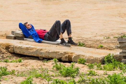 Belarus, Minsk - May 28, 2020: Young worker guy on a break resting, sleeping on an old concrete slab at a construction site